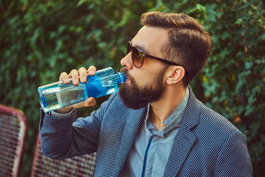  A stylish man sipping water or holding a water bottle with shiny, healthy hair. 