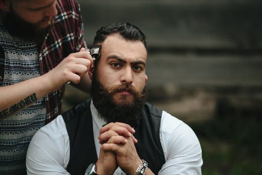 Man with a full, thick beard sitting in a barber chair while getting a trim