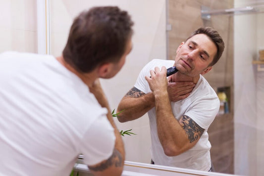 Man using a handheld trimmer to clean up neckline in the mirror